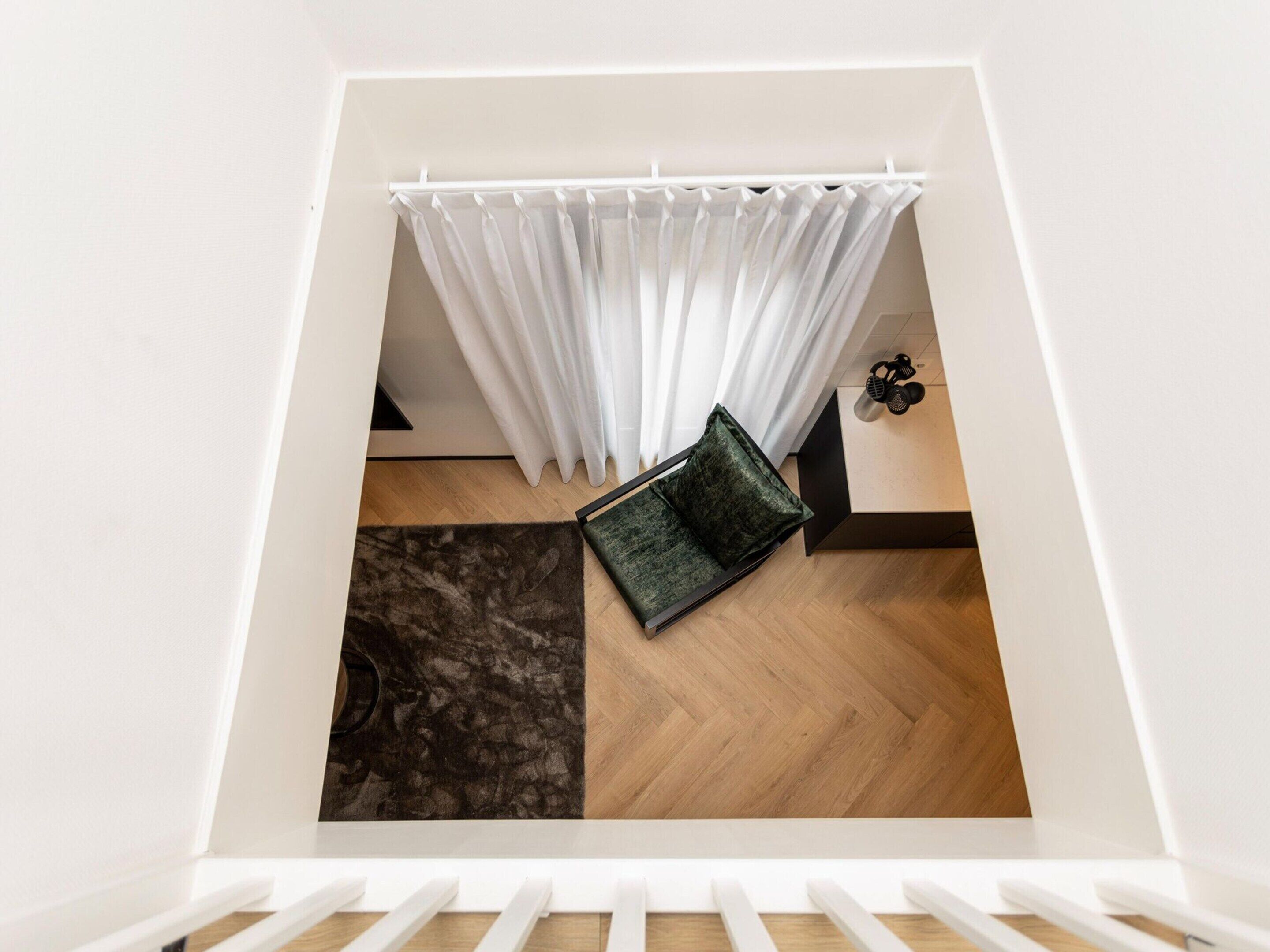 Un dormitorio tipo loft moderno con techo blanco, suelo de madera, sofá negro y cortina blanca.