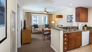 Une chambre d’hôtel avec une kitchenette, un coin repas comprenant un canapé et des fauteuils, et une vue sur le paysage urbain.