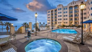Un espace piscine d’hôtel comprenant des chaises longues, un jacuzzi et un bâtiment doté de balcons.