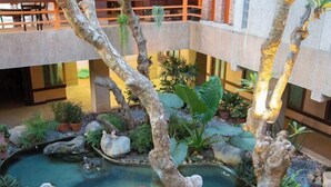 Un jardín interior con estanque de peces koi, adornos de piedra y diversas plantas.