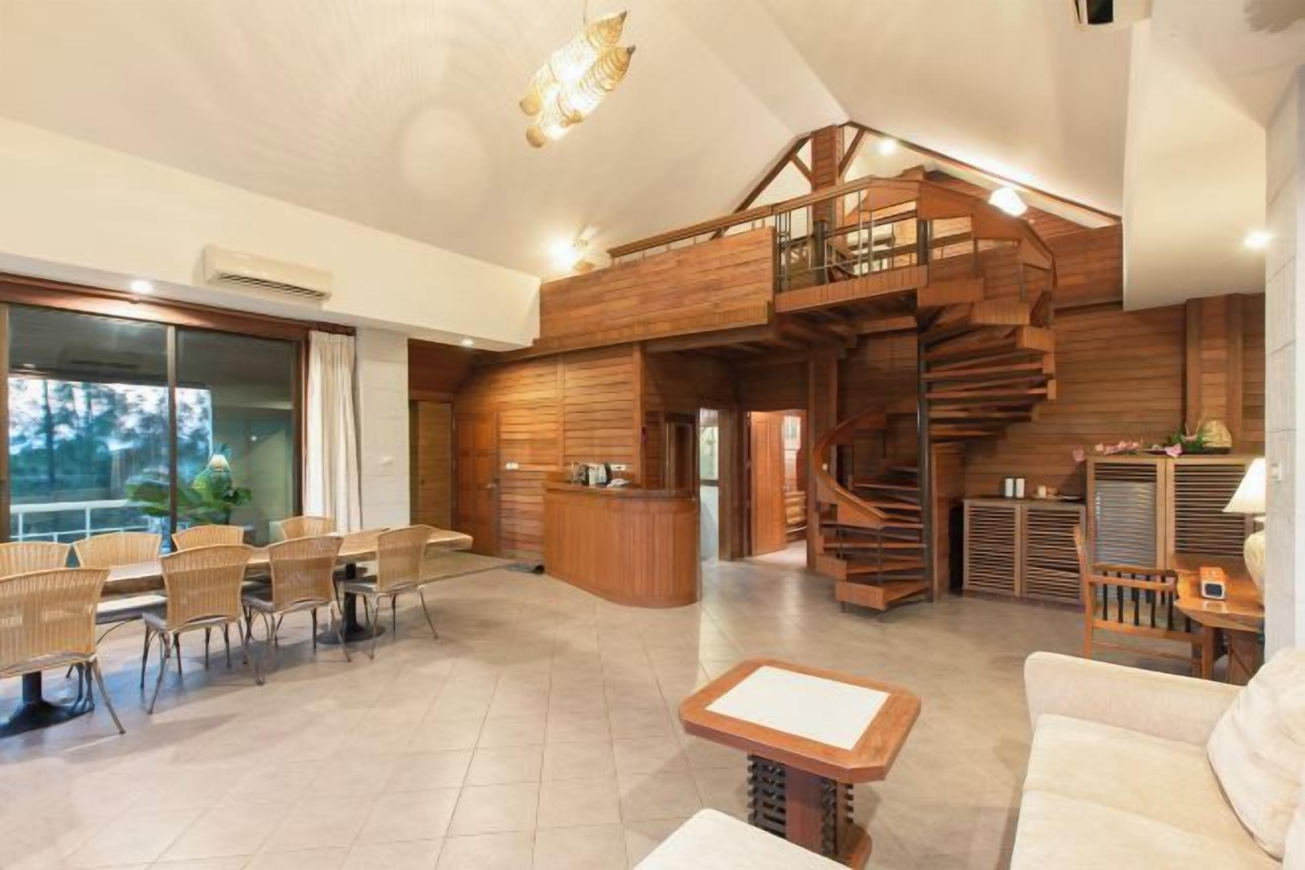 A spacious living area with a wooden staircase, a reception desk, and a dining area with wicker chairs.