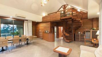 A spacious living area with a wooden staircase, a reception desk, and a dining area with wicker chairs.