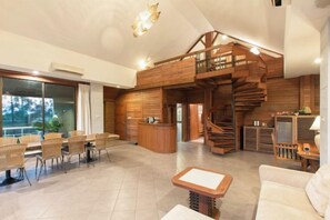 A spacious living area with a wooden staircase, a reception desk, and a dining area with wicker chairs. - Parntel Khao Yai (Pak Chong)