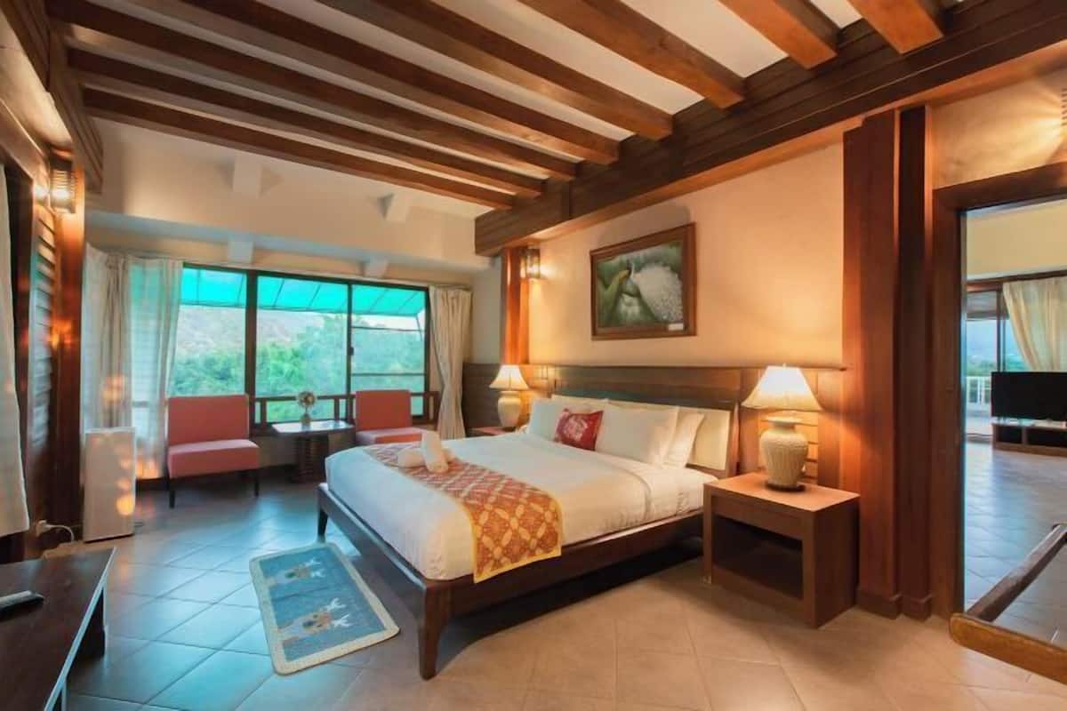 A hotel room with a large bed, two bedside tables with lamps, a window with curtains, a painting on the wall, and a view of the outdoors.