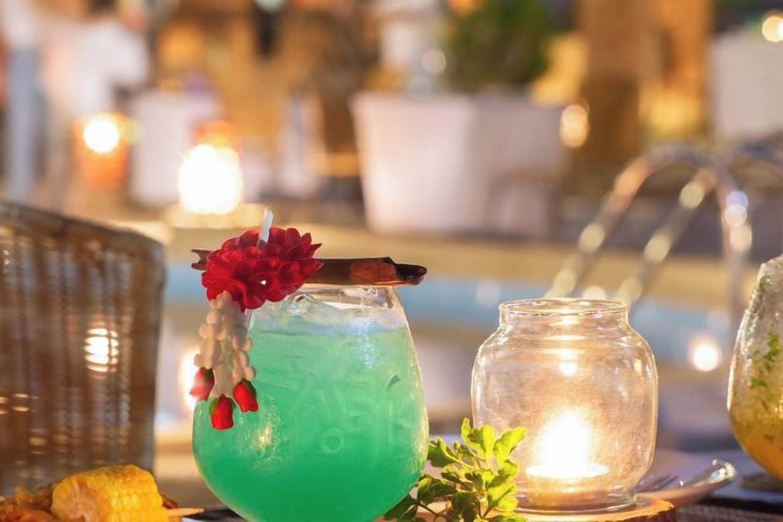 Cocktail-drinkki, jossa on kukka koristeena, tarjoiltuna pöydällä, jonka päällä on kynttilä ja lasipurkki.