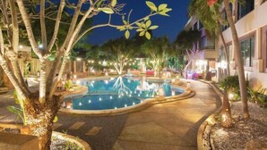 Un área de piscina nocturna con una piscina circular, rodeada de árboles e iluminada con luz ambiental.
