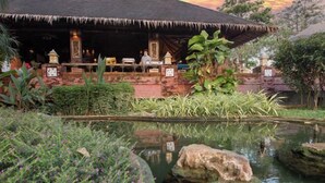 Un restaurante con techo de paja, mesas al aire libre y un estanque con rocas.