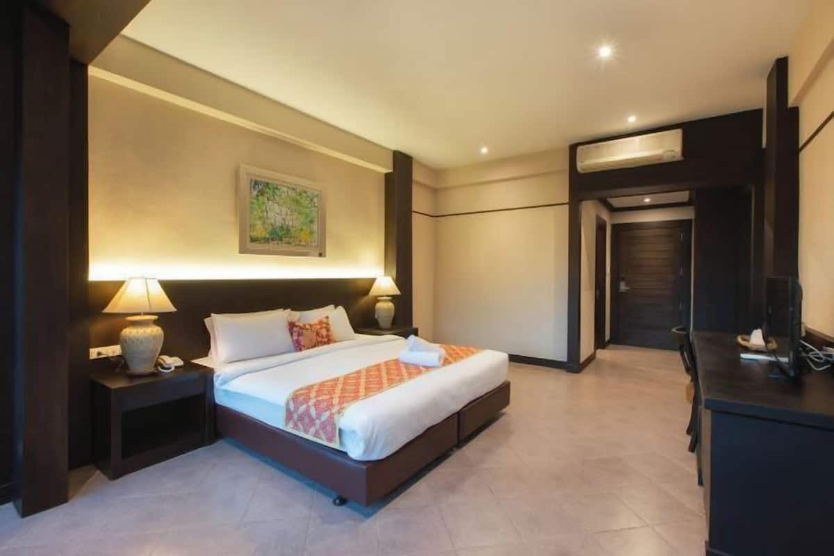 A hotel room with a bed, bedside lamps, a painting on the wall, a desk, and a wardrobe.