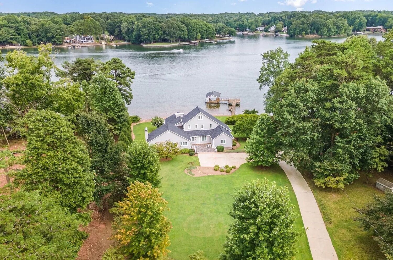 A large house with a well-maintained lawn and a dock extending into a lake, surrounded by dense trees.