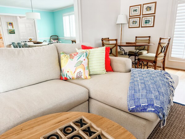 A living room with a sectional sofa, a coffee table, and a dining area with chairs and a table. - Relaxing Lakefront Home with Brand New Dock and Immaculate Vibes (Troutman)