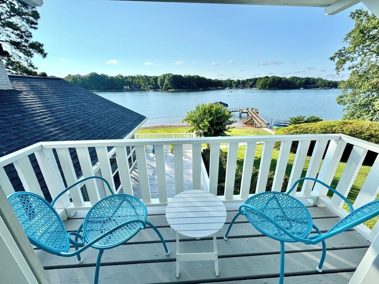 Un balcon avec une balustrade blanche, une petite table ronde et deux chaises bleues.