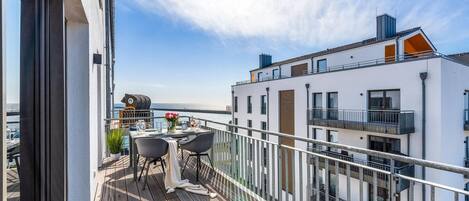 A balcony with a table and chairs, overlooking a body of water and adjacent buildings.
