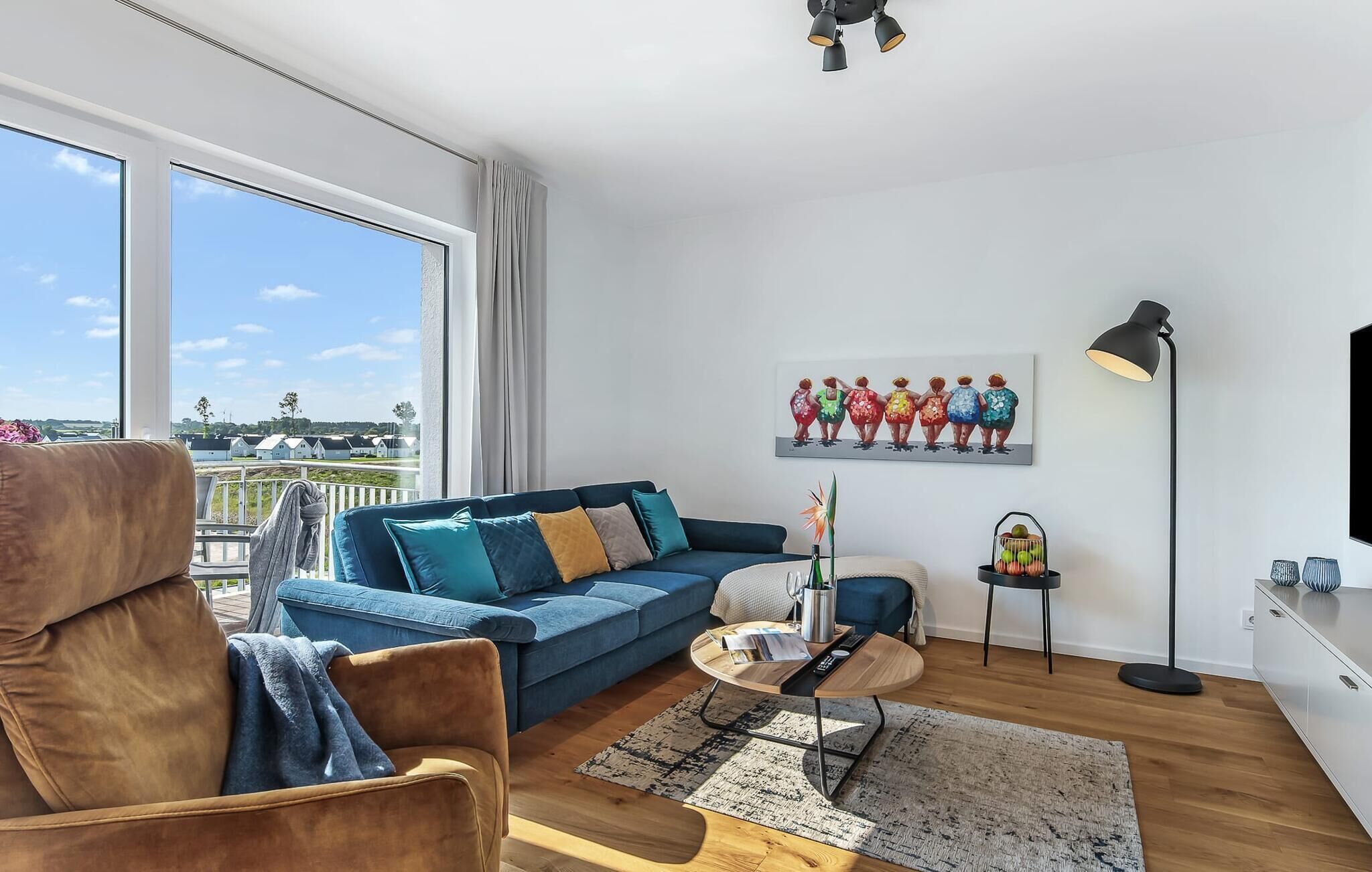A modern living room with a blue sofa, a brown armchair, a coffee table, and a painting of colorful figures.