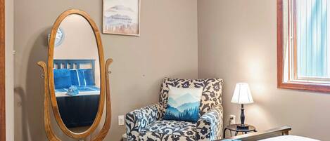 Une chambre à coucher avec un lit, une chaise, un miroir, une lampe et une fenêtre.