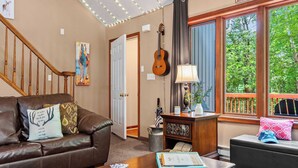 A cozy living room with a brown leather couch, a wooden coffee table with playing cards, a lamp, and a guitar.