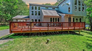 A two-story house with a deck, surrounded by trees.