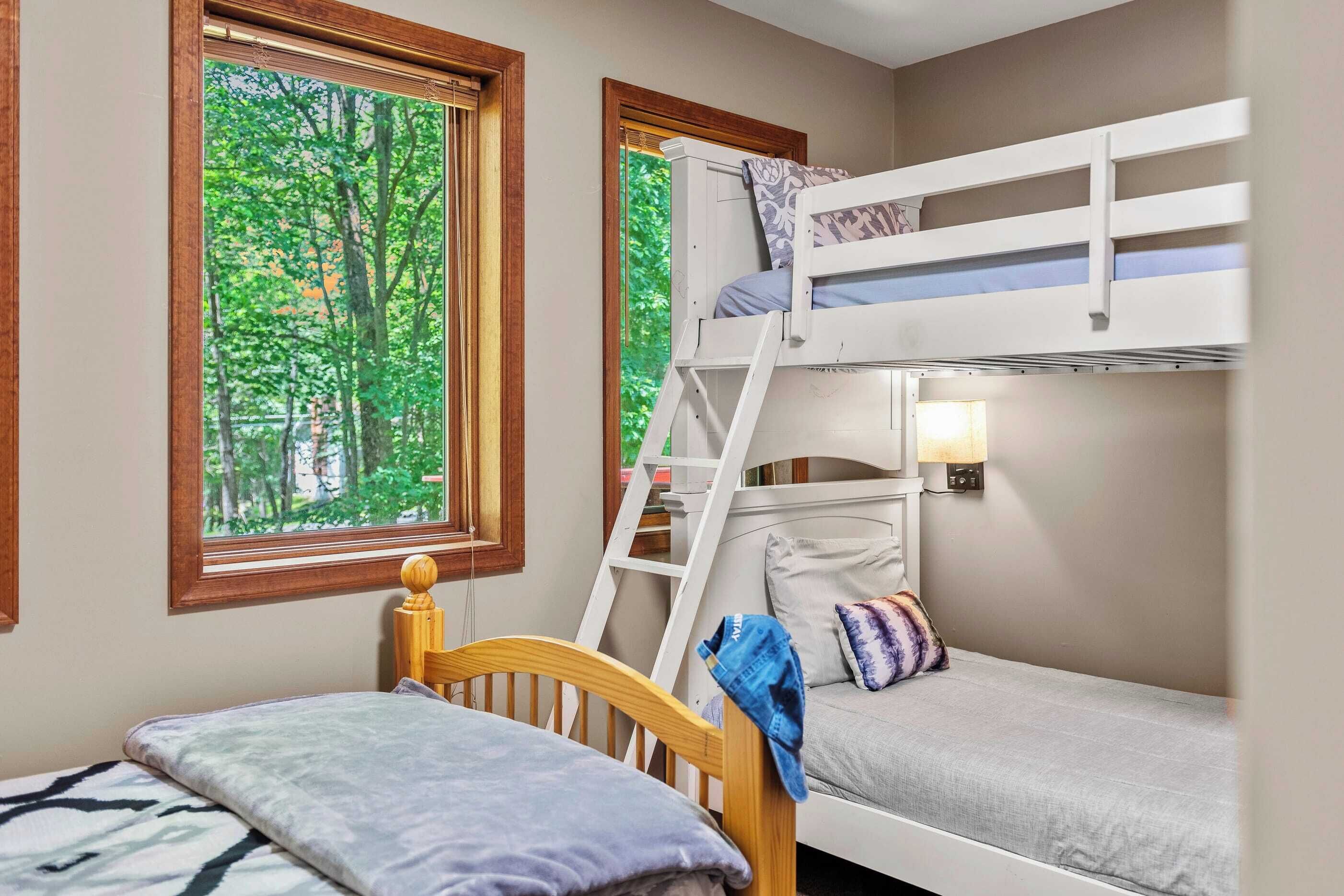 A room with bunk beds, a wooden ladder, and a window with a view of trees.