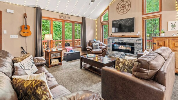 A cozy living room with leather sofas, a fireplace, and large windows offering a view of the outdoors.