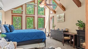 A bedroom with a large bed, a desk, a fireplace, and multiple windows.