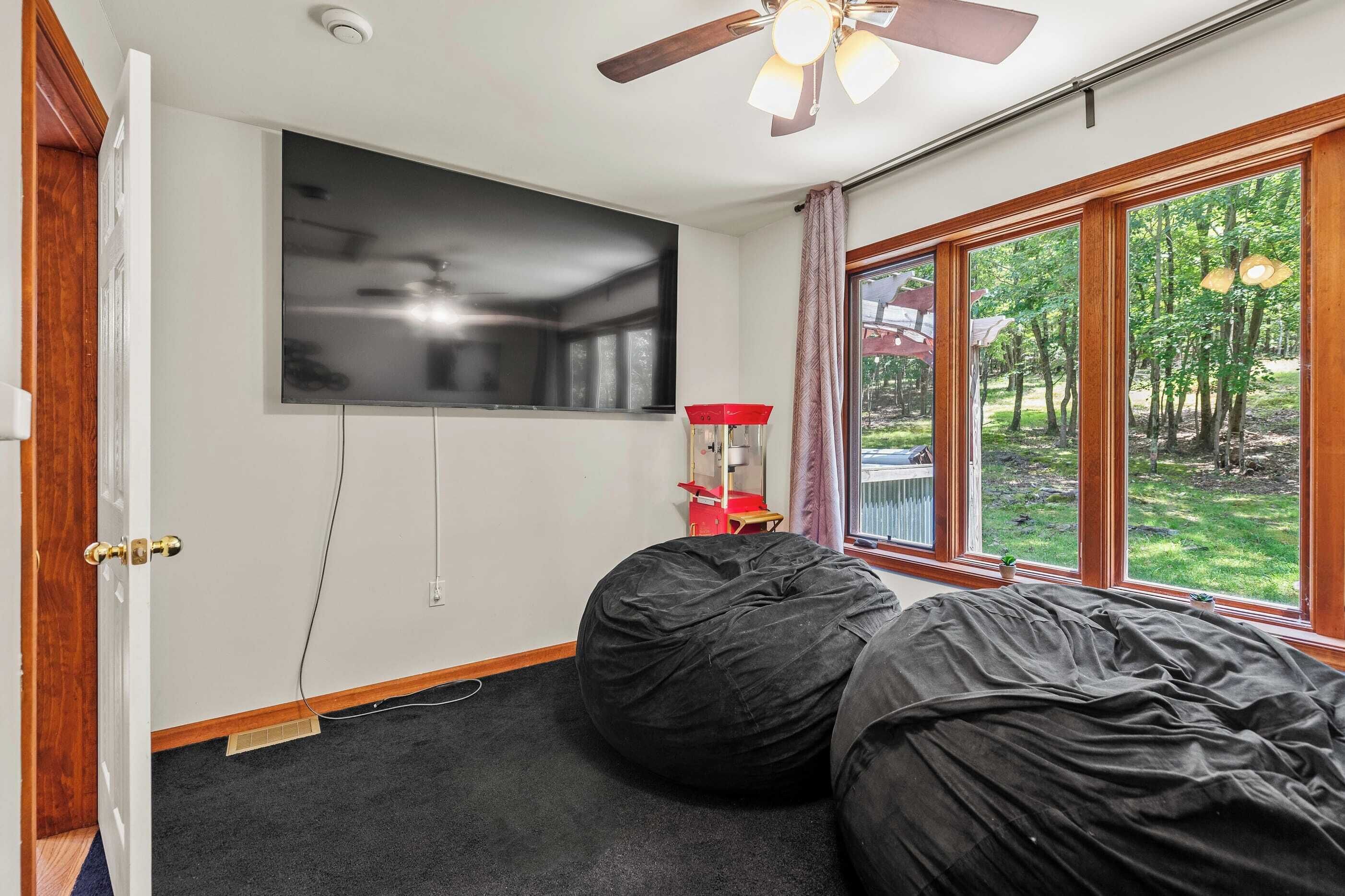 Een kamer met een groot raam, een plafondventilator, een flatscreen-tv en een kruipzak.