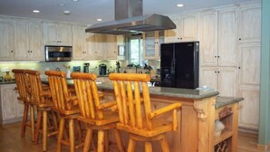 A kitchen with wooden bar stools, a stainless steel range hood, and a black refrigerator.