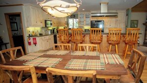 A dining area with a wooden table and chairs, a pendant light, and a kitchen in the background.