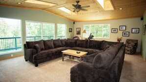 A spacious living room with a large sectional sofa, a wooden coffee table, and a ceiling fan.
