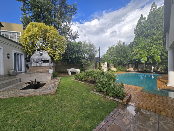 A backyard with a swimming pool, a barbecue area, and a statue.