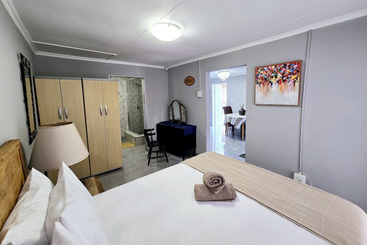 Habitación de hotel con cama, escritorio, silla, armario y baño con ducha.