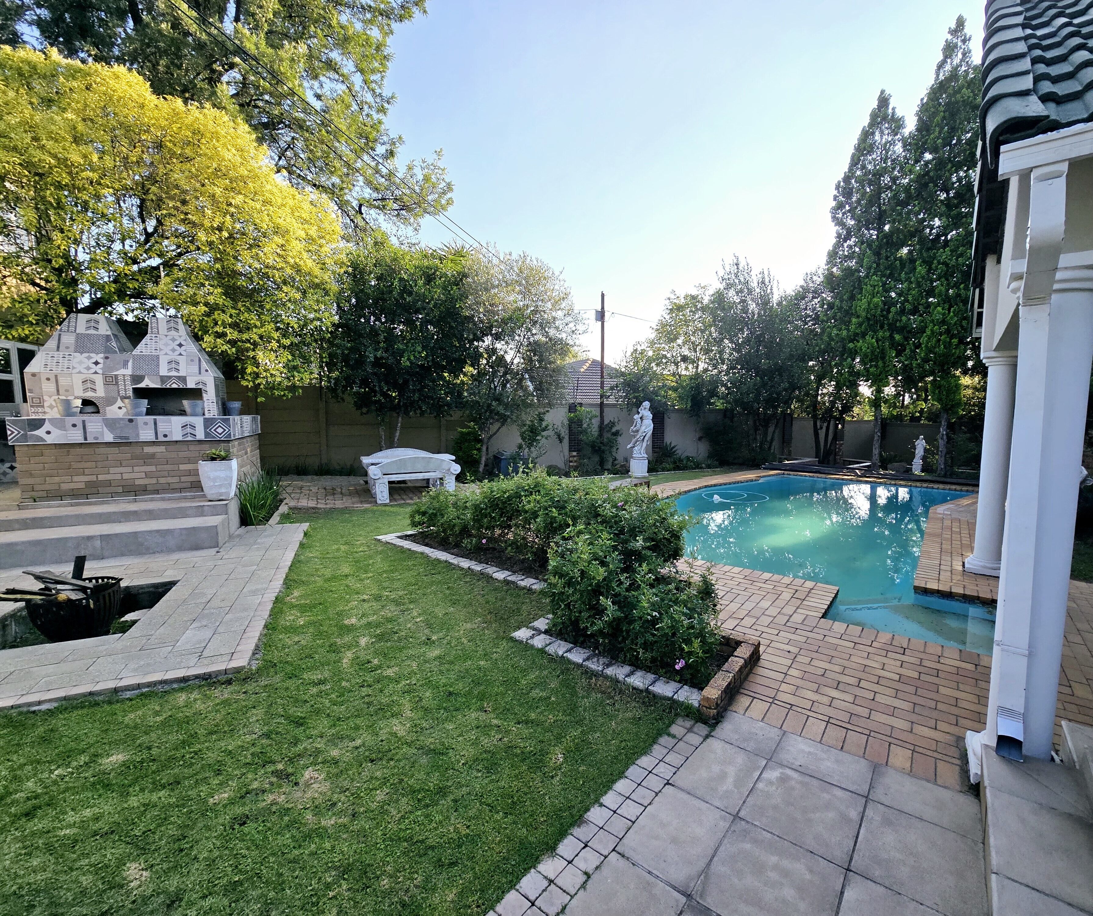 A backyard with a swimming pool, a barbecue area, and a statue.