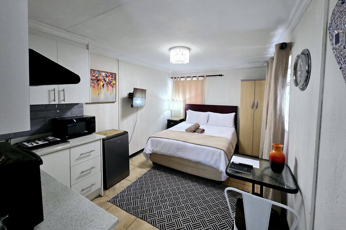Habitación de hotel pequeña con cama, escritorio con silla, microondas, refrigerador pequeño y televisor.