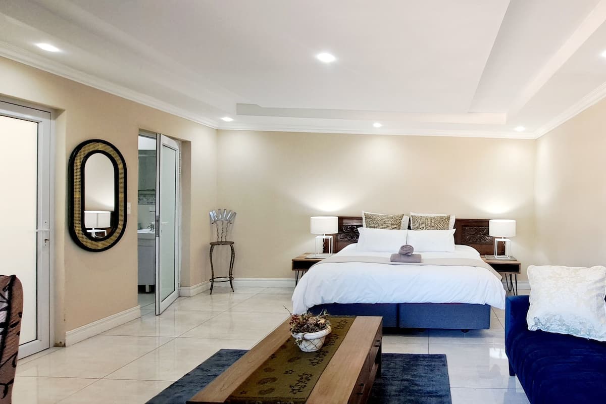 Habitación de hotel moderna con una cama grande, un sofá azul, una mesa de centro de madera y un espejo en la pared.