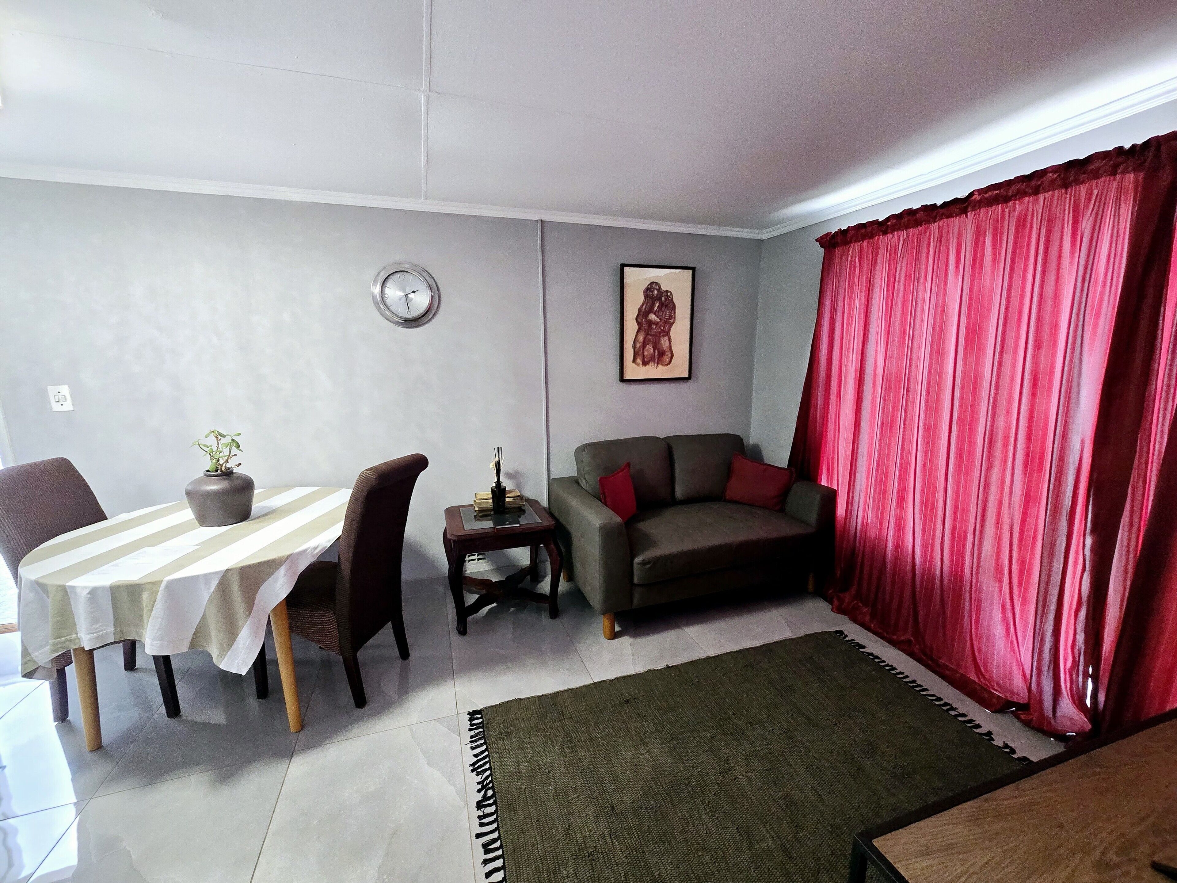 Una sala de estar con una mesa de comedor, un sofá, un reloj y un cuadro en la pared.