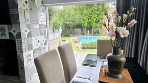 Un comedor con vistas a una piscina, mobiliario exterior y un jarrón con flores.