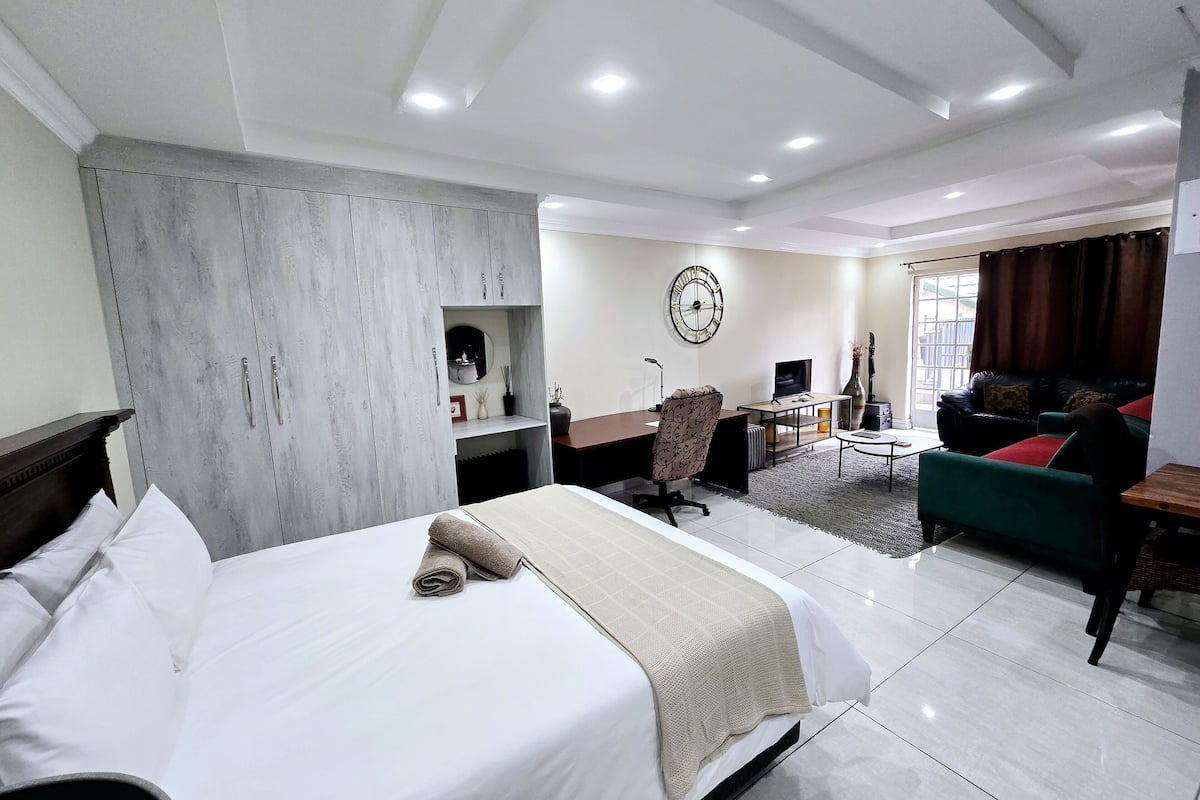 Una habitación de hotel con cama, escritorio, sillón, sofá y un espejo grande.