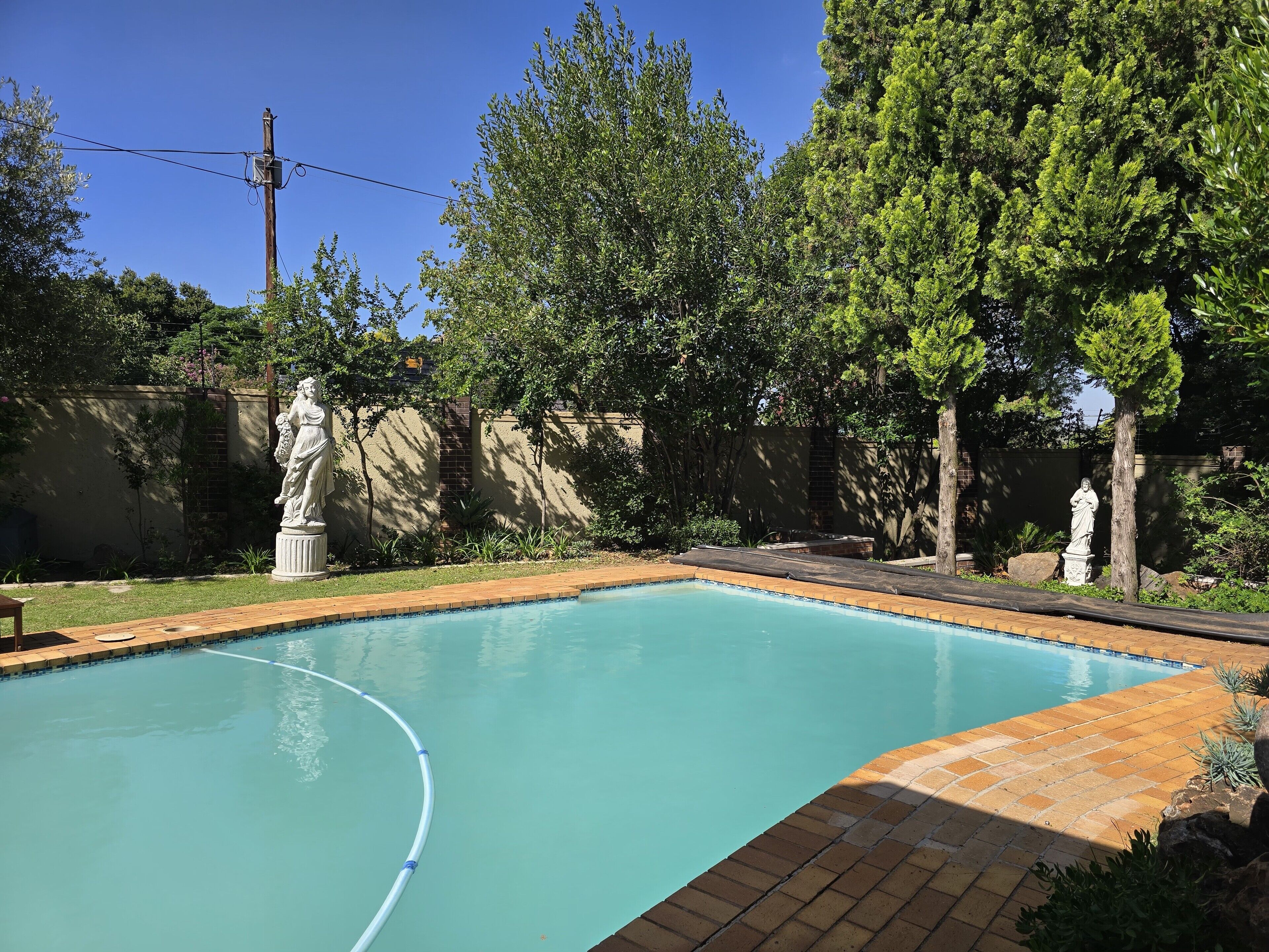 A swimming pool with statues, surrounded by trees and a brick wall.