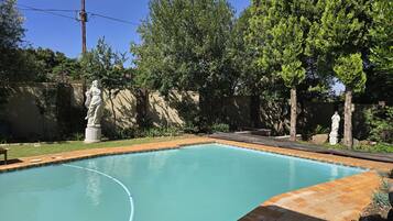 A swimming pool with statues, surrounded by trees and a brick wall.