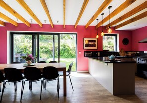 Une cuisine moderne avec des poutres en bois, un coin repas avec une table et des chaises, et de grandes fenêtres.