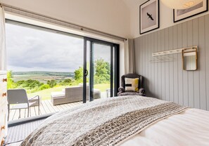 Ein Schlafzimmer mit einem großen Bett, Ausblick ins Freie, einem Sessel und einem Spiegel an der Wand.
