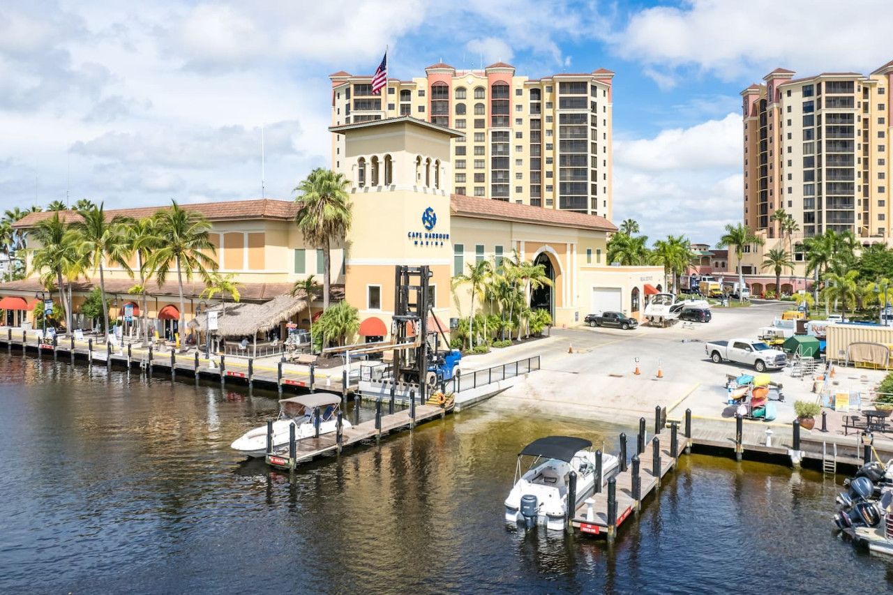 A marina with boats docked, a hotel with a flag, and palm trees.
