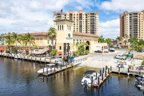 A marina with boats docked, a hotel with a flag, and palm trees.