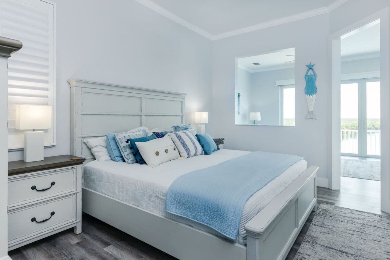 A bedroom with a white bed, bedside tables, and a large window.
