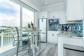 A modern kitchen with a large window, a refrigerator, a microwave, and a dining area with a table and chairs.