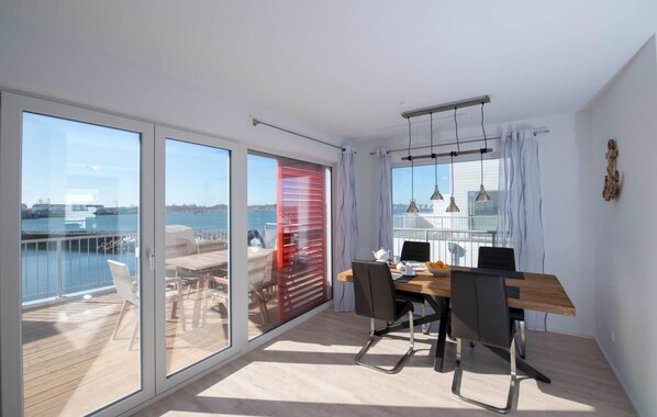 Un comedor moderno con vistas al agua, grandes puertas correderas de vidrio y un balcón con mobiliario exterior.