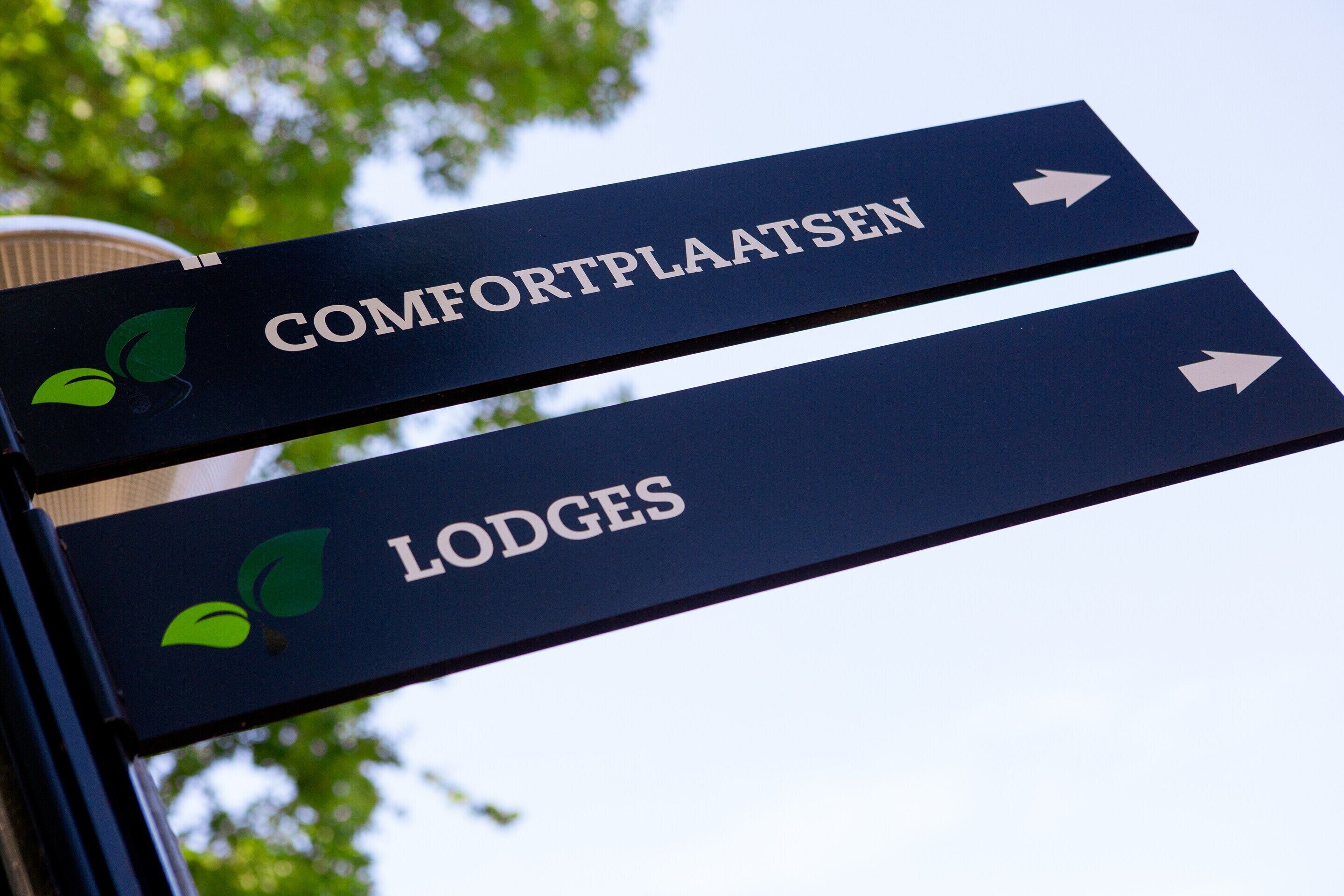 Señales direccionales para 'Comfortplaatsen' y 'Lodges' con flechas indicando la dirección.