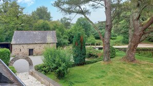 A stone building with a sloped roof, surrounded by lush greenery and trees. - Lovely home in Saint-Thurien with WiFi (Saint-Thurien)