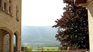 Un patio con columnas de piedra, una mesa y sillas, y vistas a un valle verde y montañas.