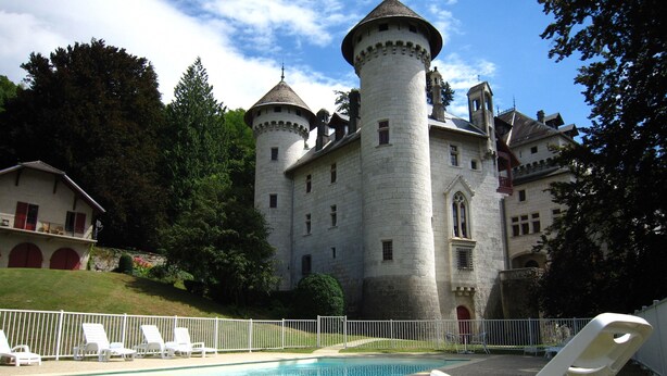 Un castillo con piscina, sillas de descanso blancas y una valla blanca.