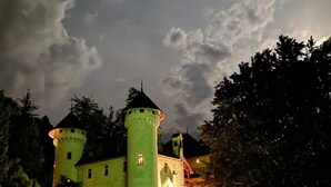 Un castillo con dos torres, un edificio principal y una entrada iluminada.