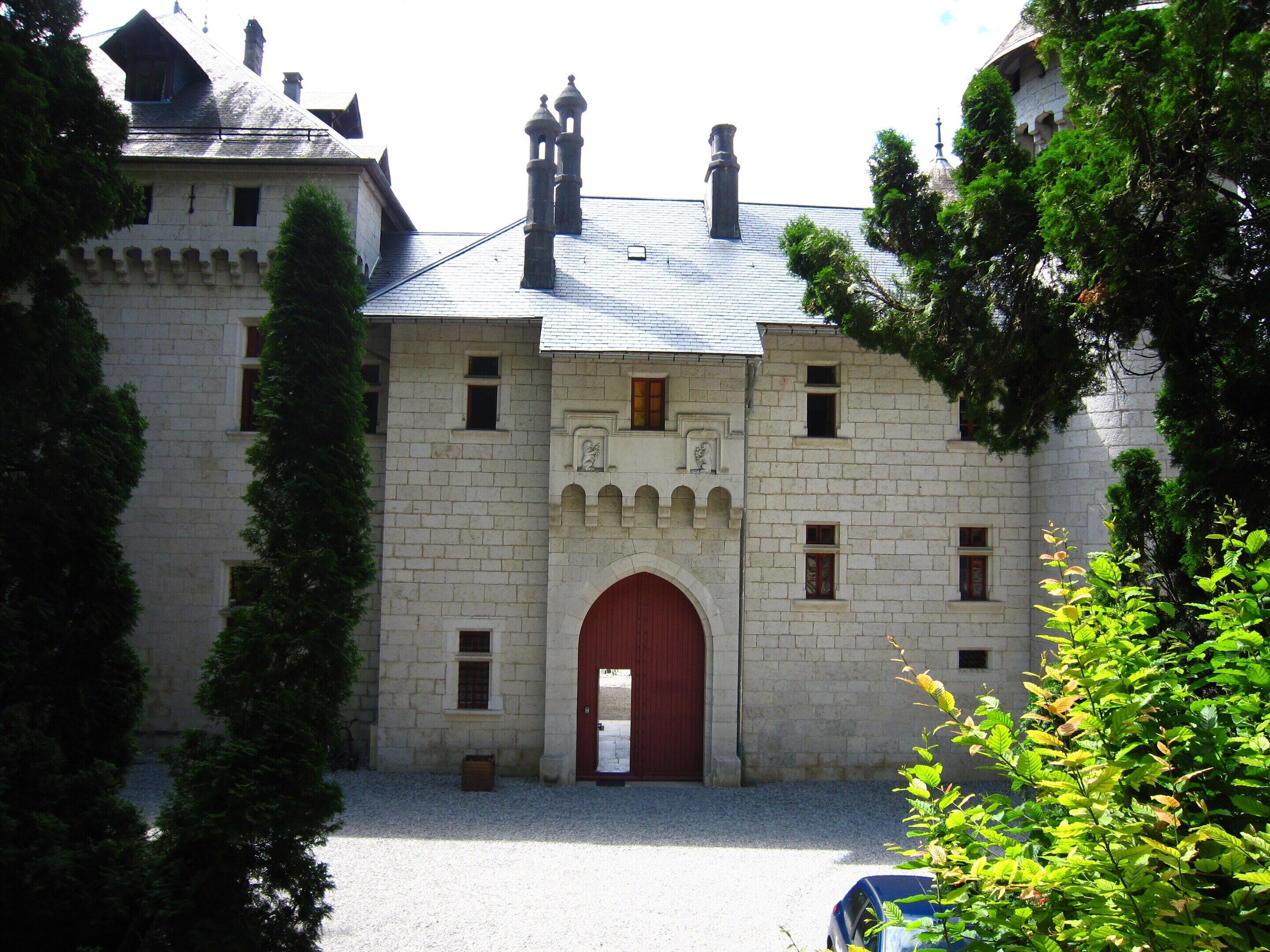 Ein historisches Steinhaus mit einem zentralen roten Bogenportal, zahlreichen Fenstern und einer symmetrischen Fassade.